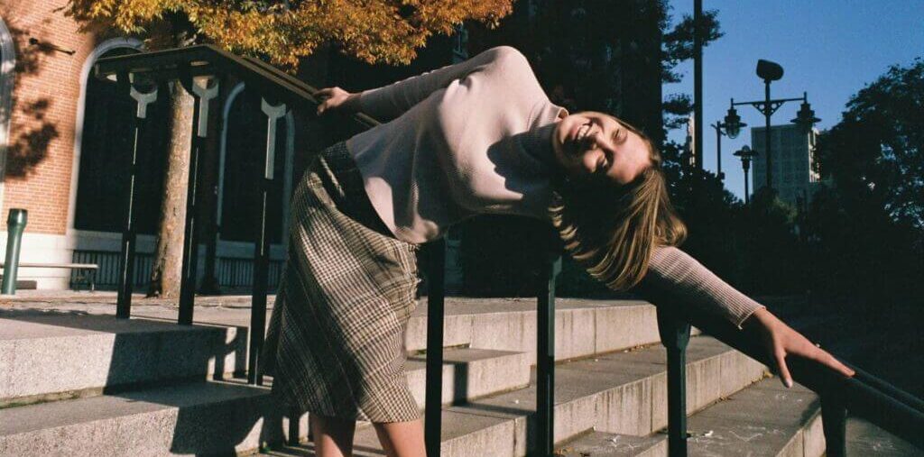 film photograph shows a young white woman walking down steps, leaning on the stair railing, outdoors