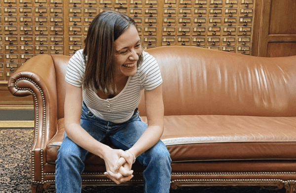 Abby Brennan, a white woman with a medium length brown bob haircut, sits on a brown leather sofa in the Yale library lobby in front of a wall of library card catalog drawers